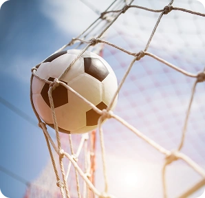 Un ballon de football coincé dans le coin supérieur des filets du but, avec le ciel bleu et le soleil en arrière-plan